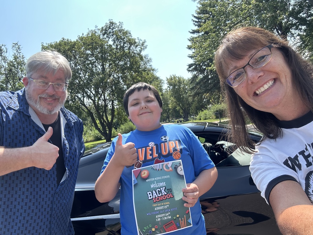 Two Whittier Middle Schools staff members stand next to an incoming student who is giving a thumbs up while holding a back to school sign. 