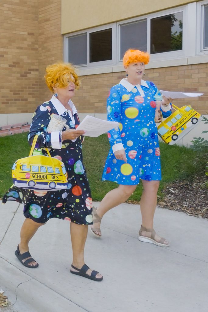 Garfield Principal Skogstad and Admin Intern Alberty walk outside Garfield dress up as Magic School Bus's Ms. Frizzle, complete with a space-temed dress and orange curly wigs as part of their Back to School Magic School Bus tour of their school neighborhood.