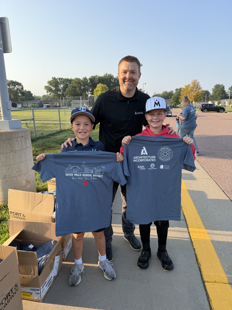 Architecture Incorporated volunteer stands smiling next to two young SFSD students who helped distribute t-shirts to staff 