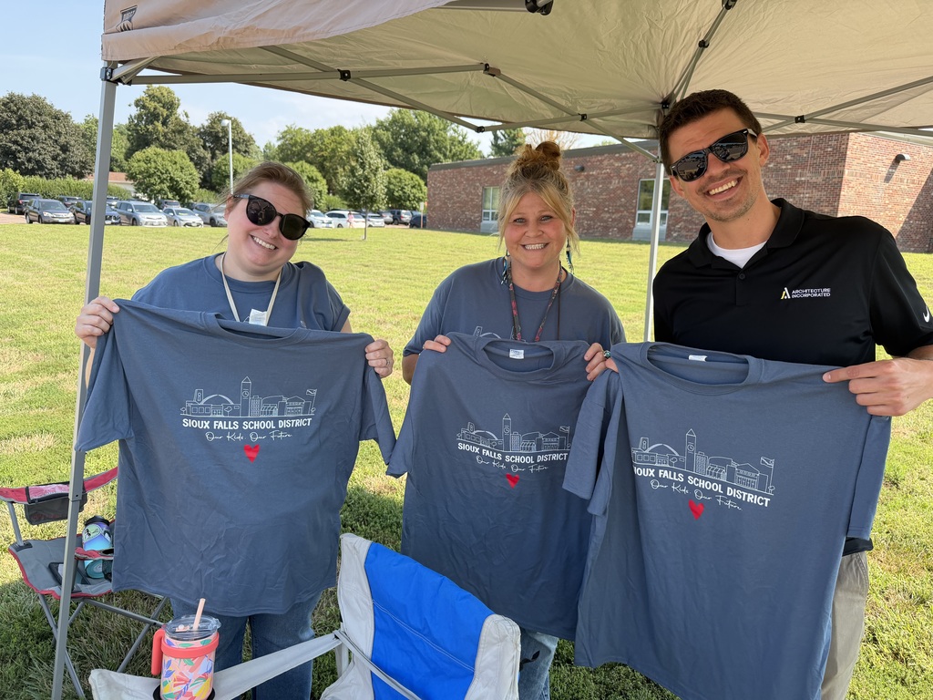 Two SFSD staff members stand next to an Architecture Incorporate volunteer holding this year's District t-shirt at a staff t-shirt distribution day