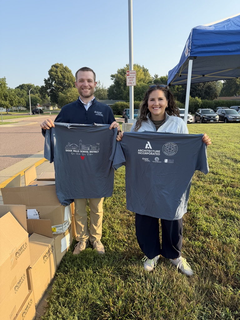 Arch Inc and Sayre Associates volunteers stand smiling holding this year's SFSD staff t-shirt at a morning staff t-shirt distribution event