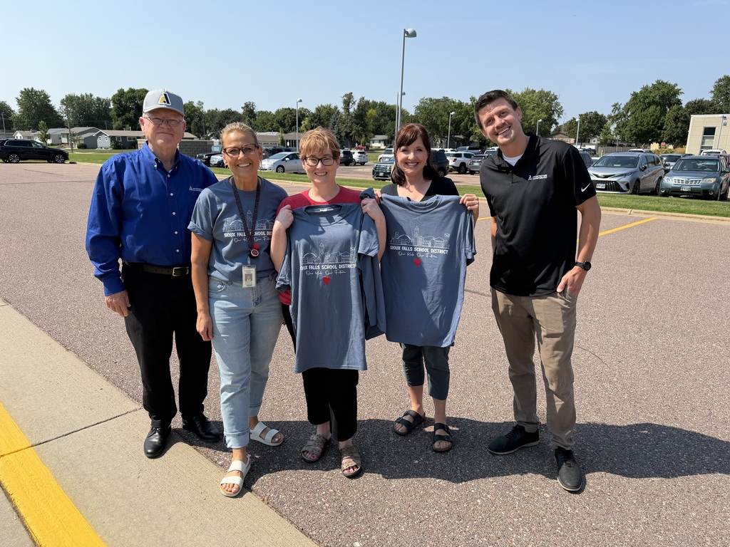 Two SFSD staff members smile holding their 2026 district t-shirts alongside volunteers from our t-shirt sponsors Architecture Incorporated and Sayre Associates