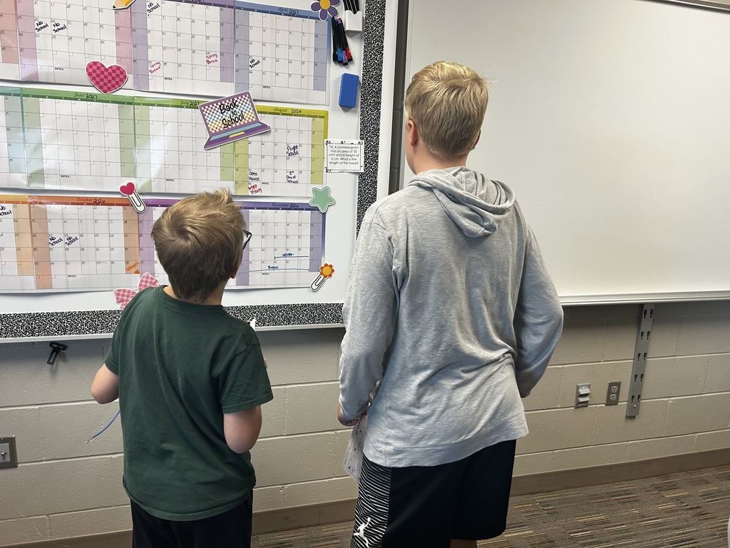 Two students solving a math problem hung up on the wall.