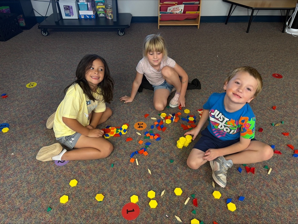 3 students on the floor making designs with shapes.