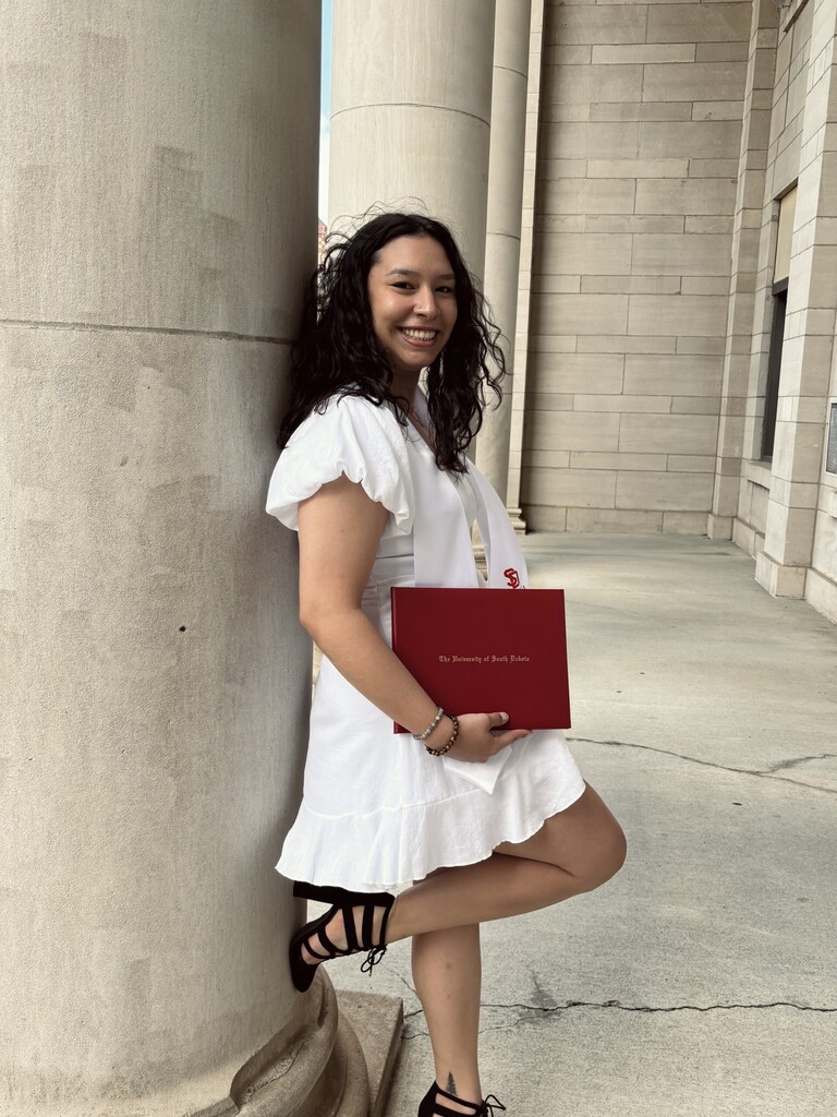 Miss West at her college graduation with her diploma.