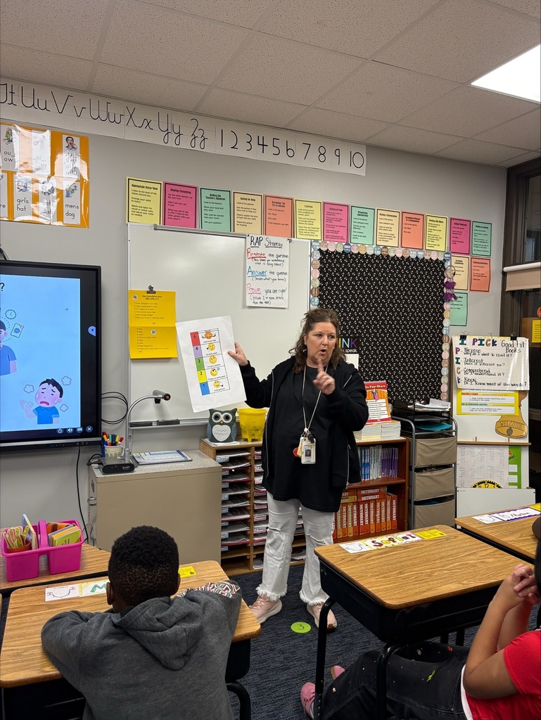 A teacher at the front of the room showing students a feelings chart for students to use to share how they are feeling