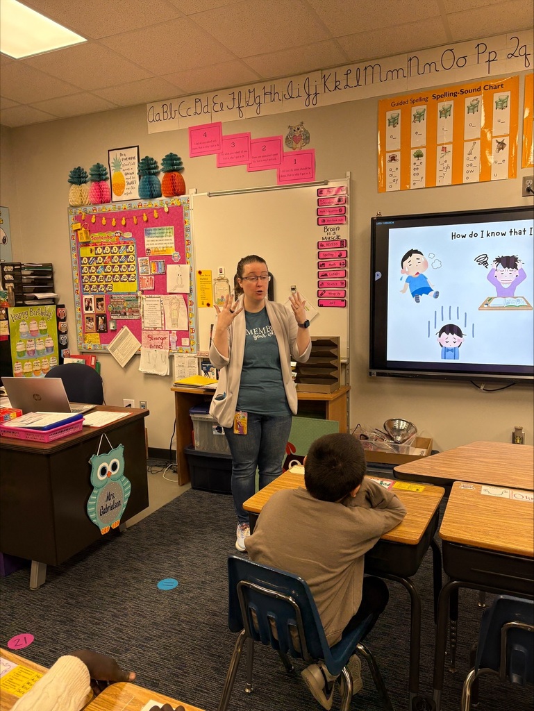 A teacher by the screen demonstrating taking deep breaths to help calm down
