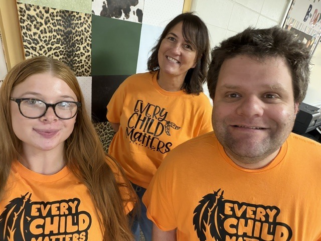 Three Memorial Middle School staff members take a selfie together, all wearing orange "Every Child Matters" T-shirts.