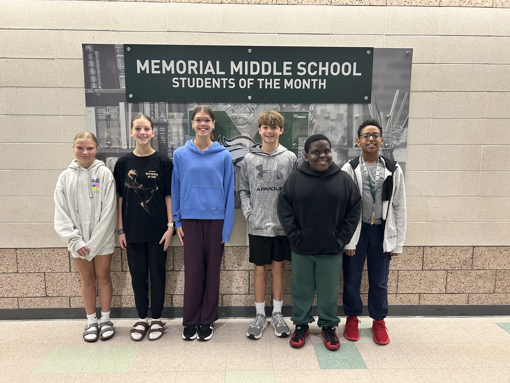 Six Memorial Middle School students standing in front of the "Memorial Middle School Students of the Month" wall sign.