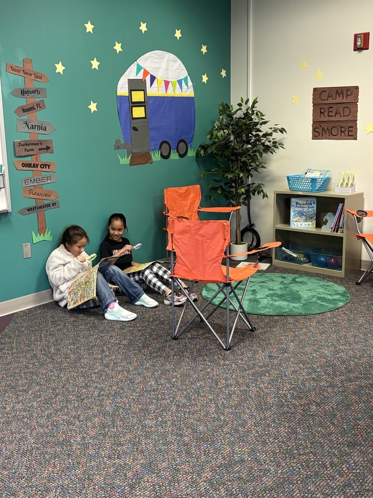 2 girls reading books along the walk by camping chairs.
