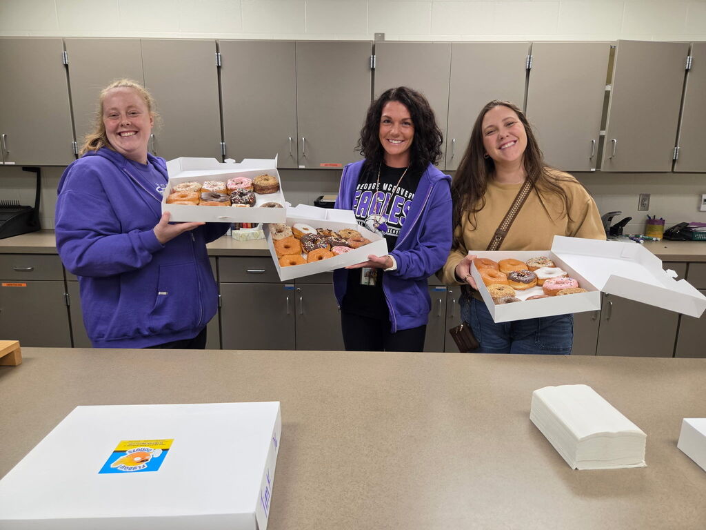 Staff holding up boxes of doughnuts. 