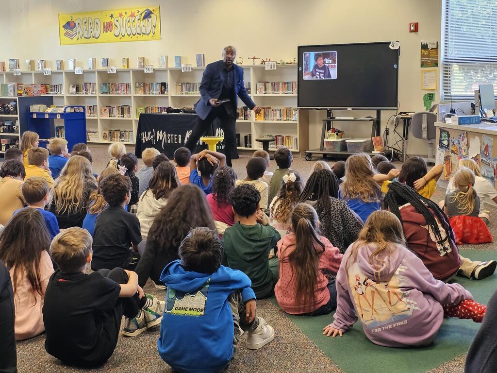 Mister Brown talking to students who are sitting on the ground.