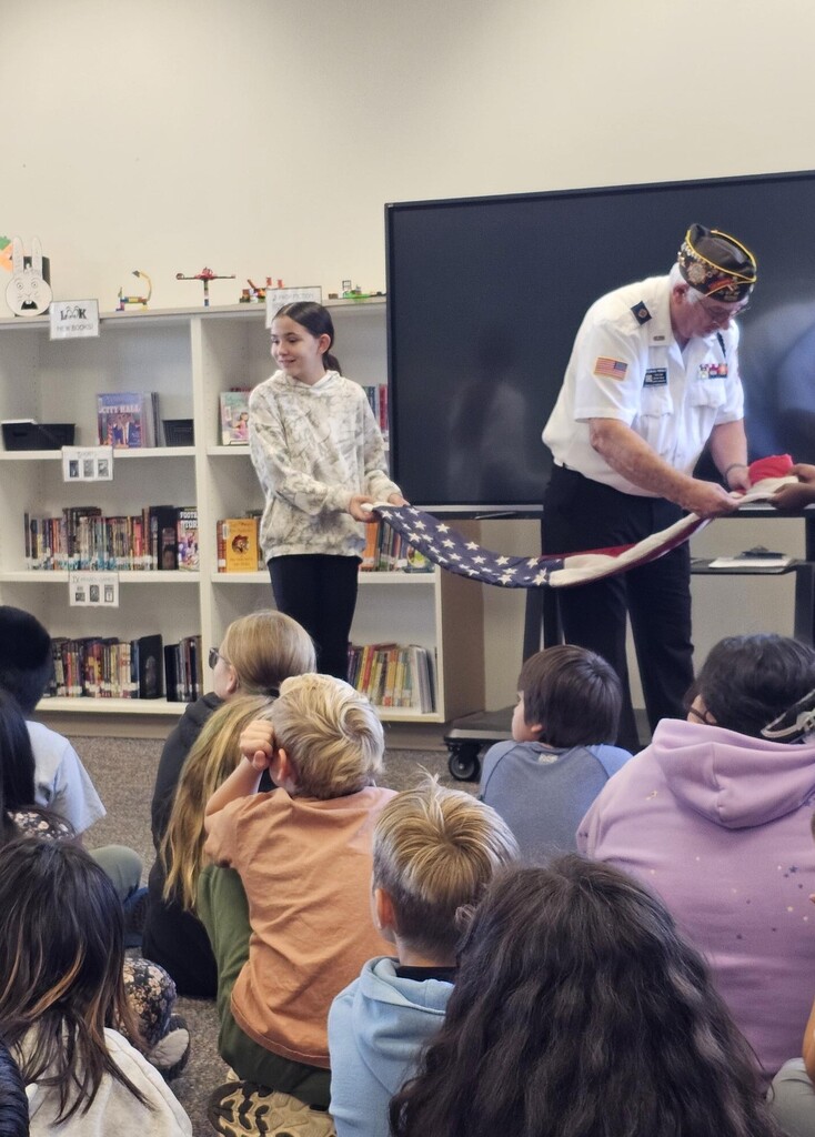 2 students folding the flag with help from a Veteran