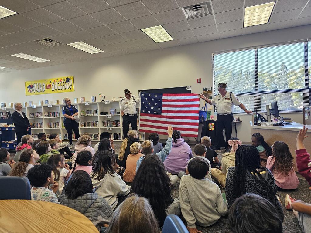 Adults showing students a flag.