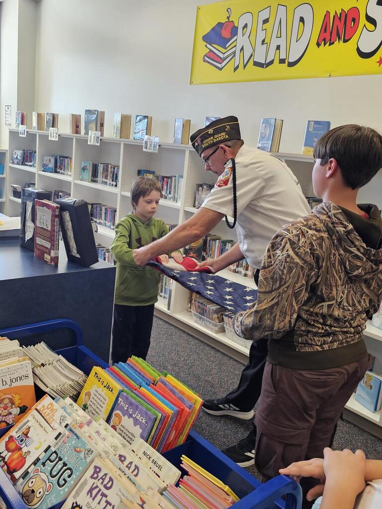 2 students folding the flag with help from a Veteran
