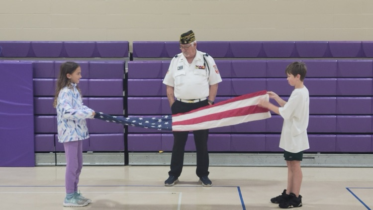 man shows two children how to fold United States flag 