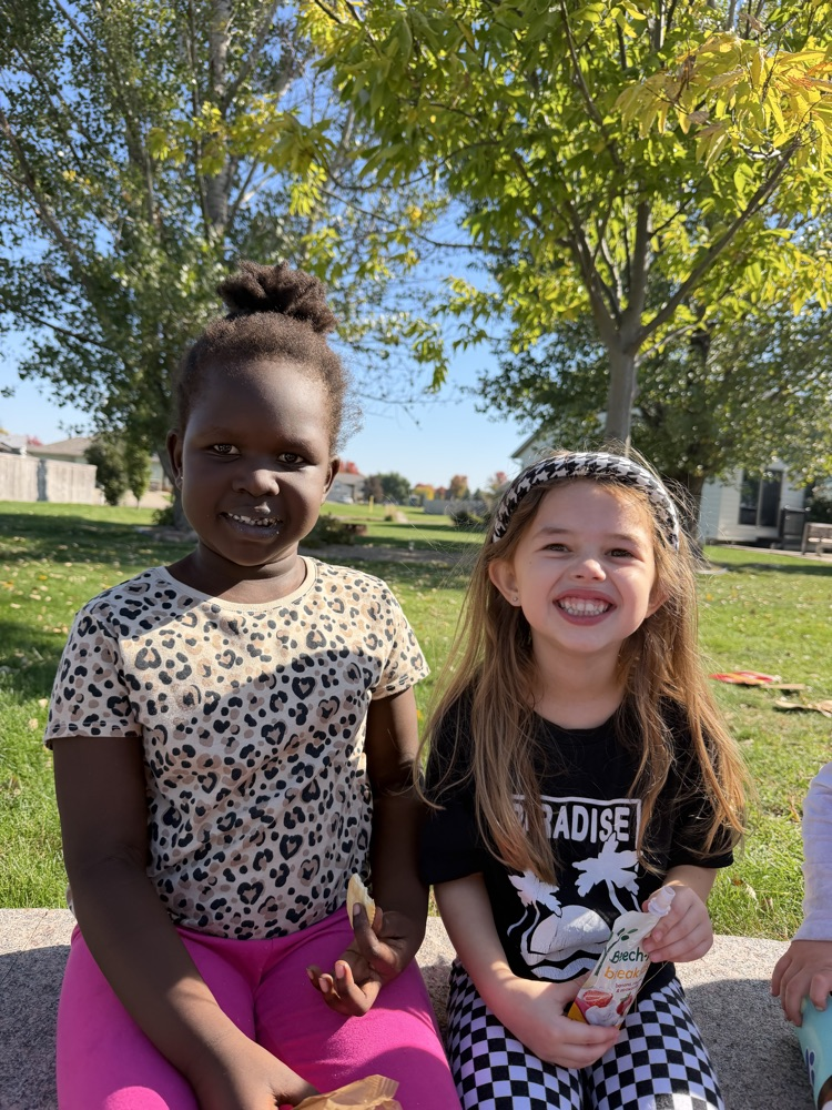 two girls sitting in an outdoor classroom having snacks 