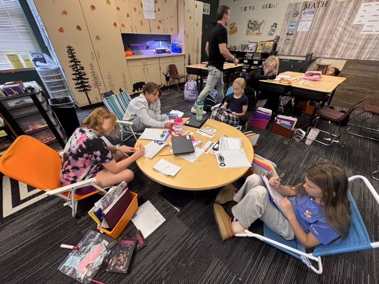 students lounging in lawn chairs around a classroom table reading books