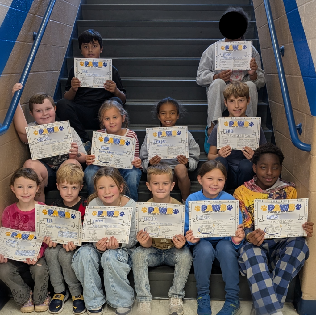 Students sitting on the stairs holding a PAWS Student of the Month certificate as they're awarded being the first PAWS Students of the month!