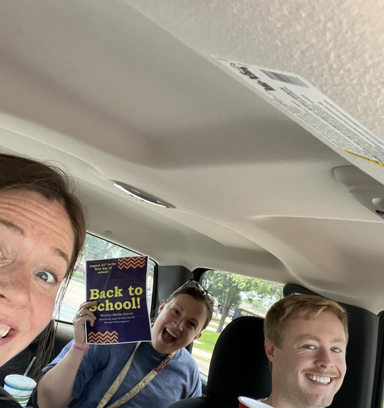 Three teachers sit in a van holding back to school signs