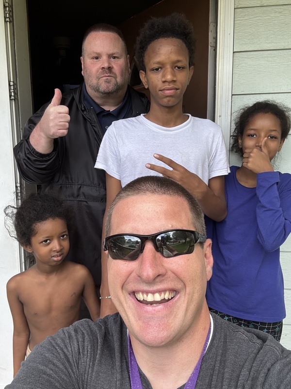 three young kids and two adults give thumbs up to the camera