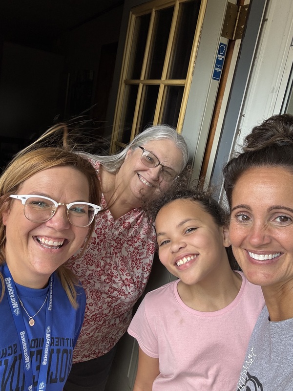 a woman and young girl stand with two teachers in their doorway smiling at the camera