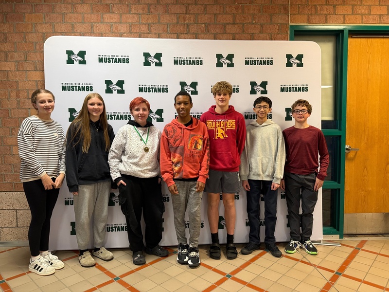 Seven smiling 8th-grade students pose in a row to celebrate being named the student of the month.