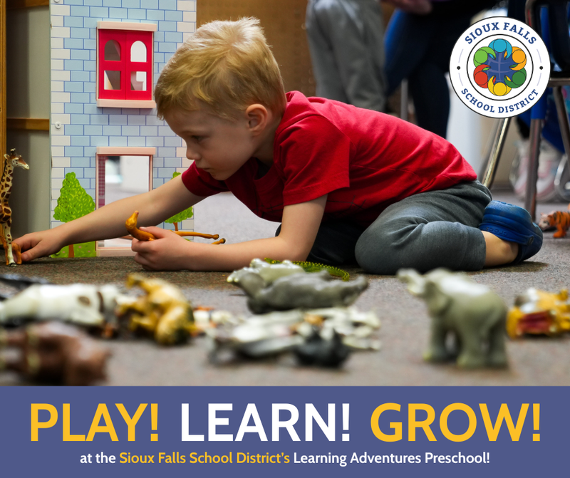 Little boy with red hair wearing a red shirt plays on the ground with toy zoo animals