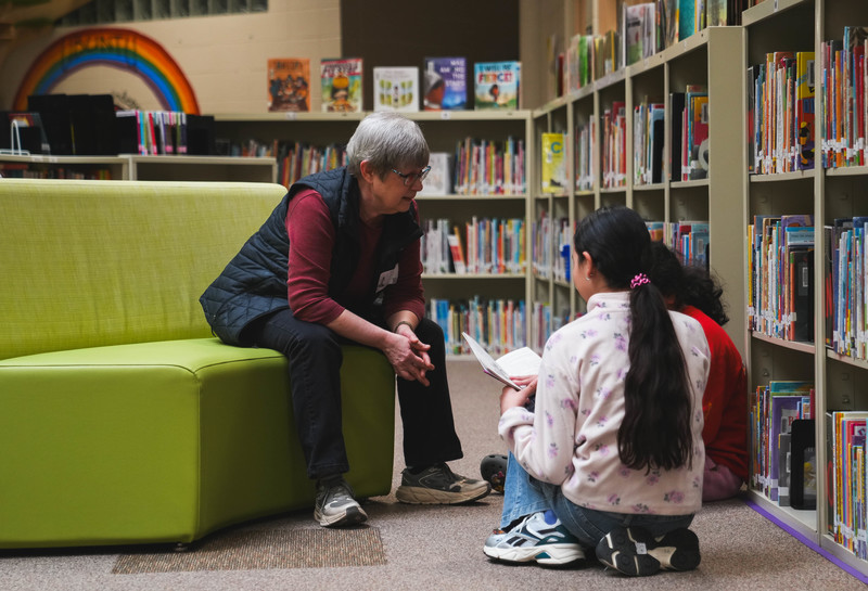 A volunteer reads to students in a library