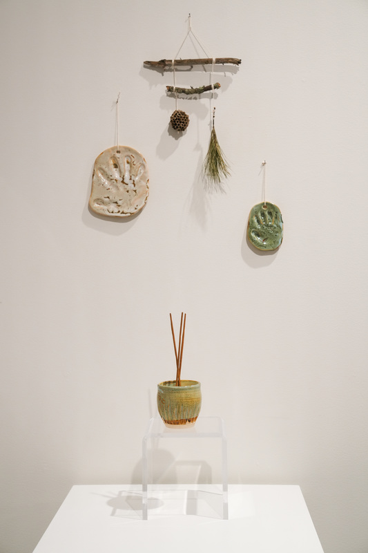 Ceramic and other multi-media works of art hang on a white wall as part of a teacher art exhibit at the Washington Pavilion