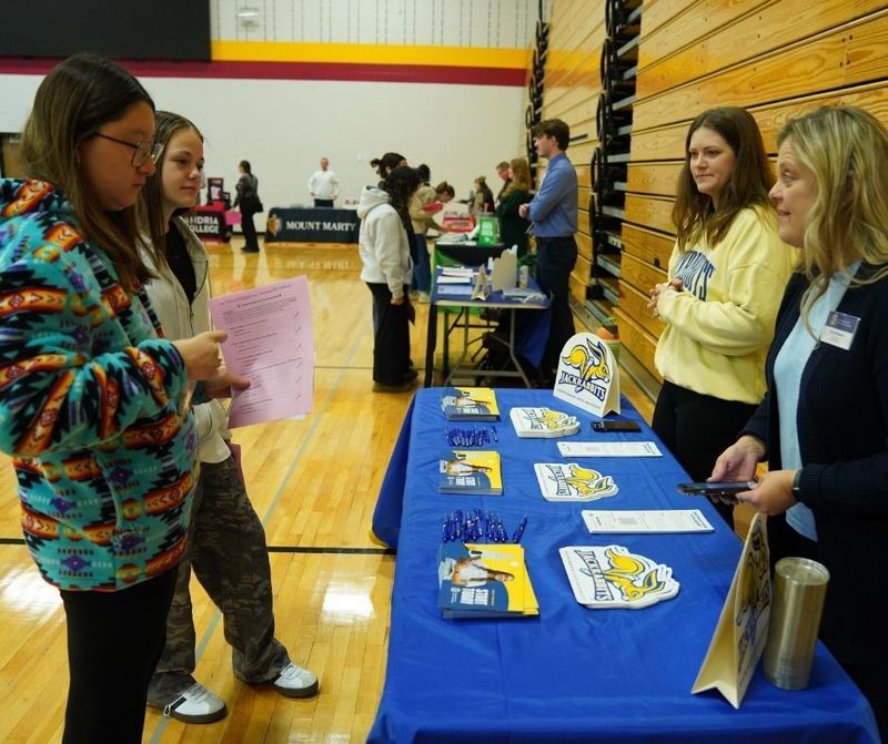 Two students stand at a college fair booth talking with a representative from SDSU