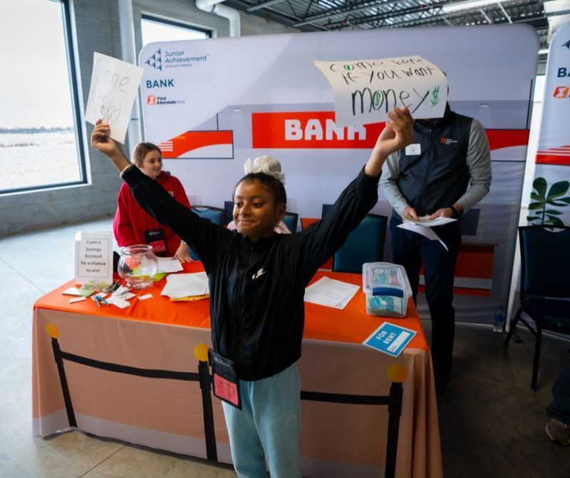 Sixth grader stands tall grinning with her arms open holding a sign that says "come here if you want money"