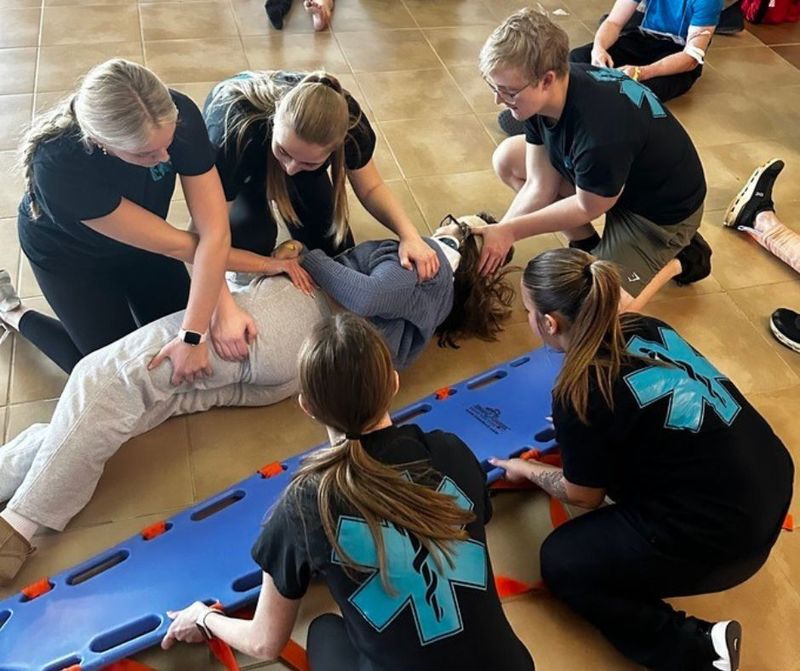 CTE health career students partake in a simulation of helping a pretend injured person on to a gurney