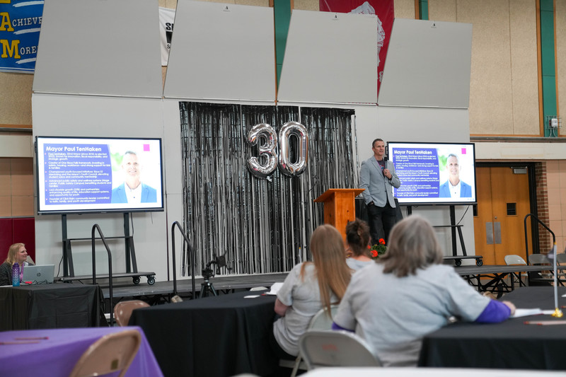 Mayor Paul TenHaken addresses a crowd from a stage with the number "30" behind him in balloon letters. 