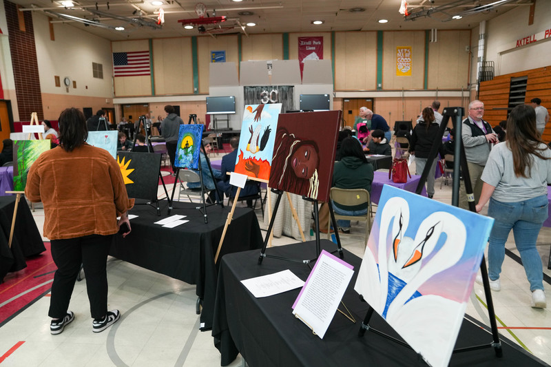 A woman looks at pieces of art on easels in a gymnasium at the 30th anniversary celebration of Joe Foss high school