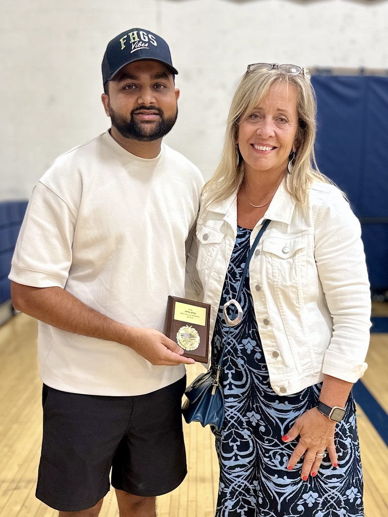 A man holding a plaque stands next to a smiling woman in a gymnasium.