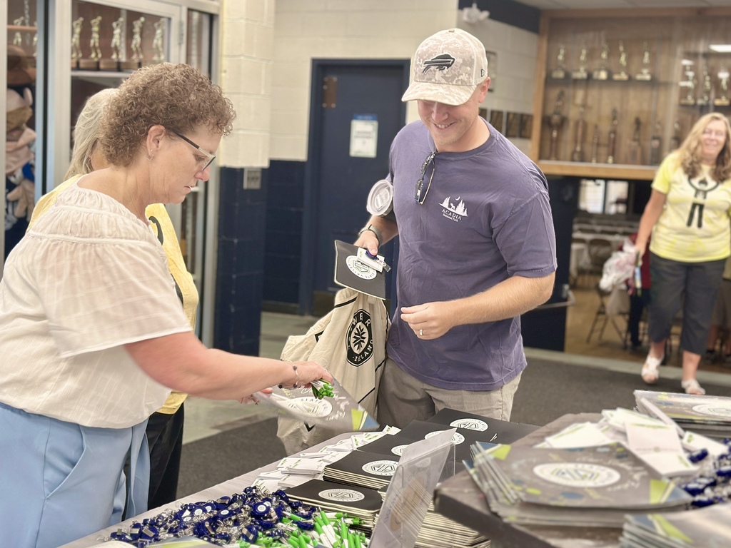 Man and woman gather Slate Valley materials from a table with pens, folders, and tote bags, smiling and engaged.