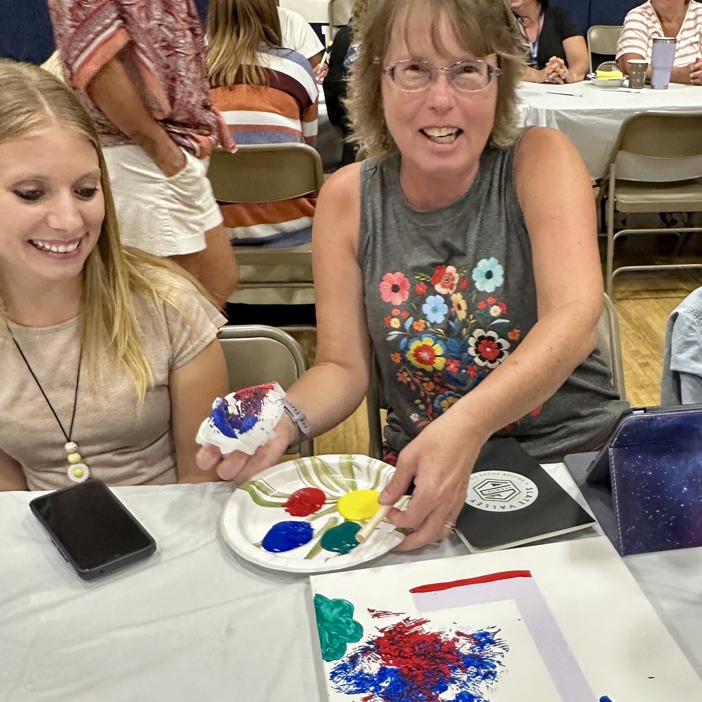 Two women smiling while painting on a paper plate with bright colors.