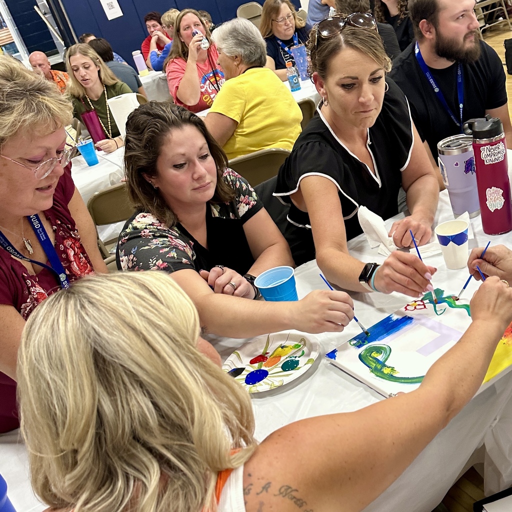 Group of women painting designs on a canvas at a shared table.
