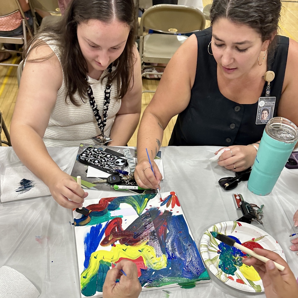 Two women painting a vibrant canvas with brushes at a table.