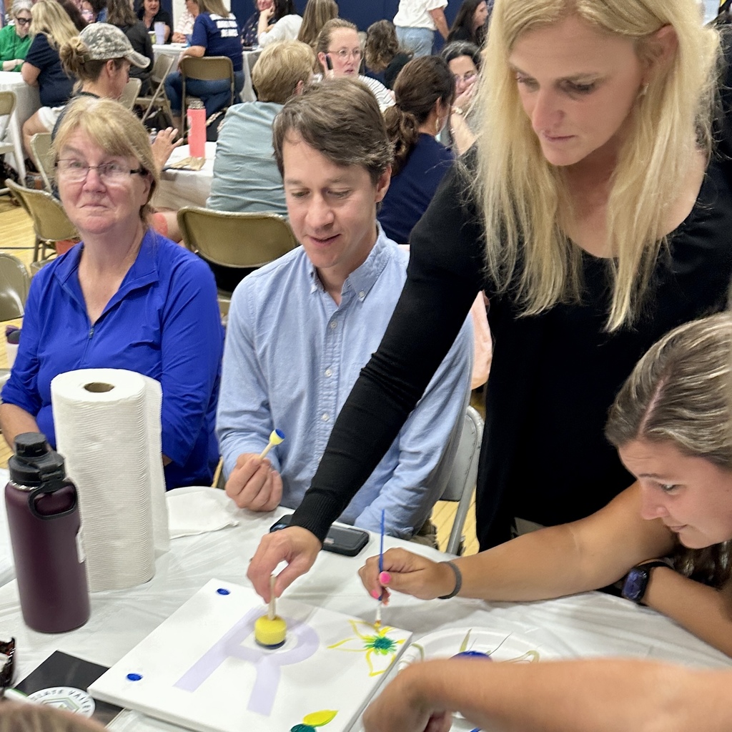 Group of people painting letters on canvases together at a table.