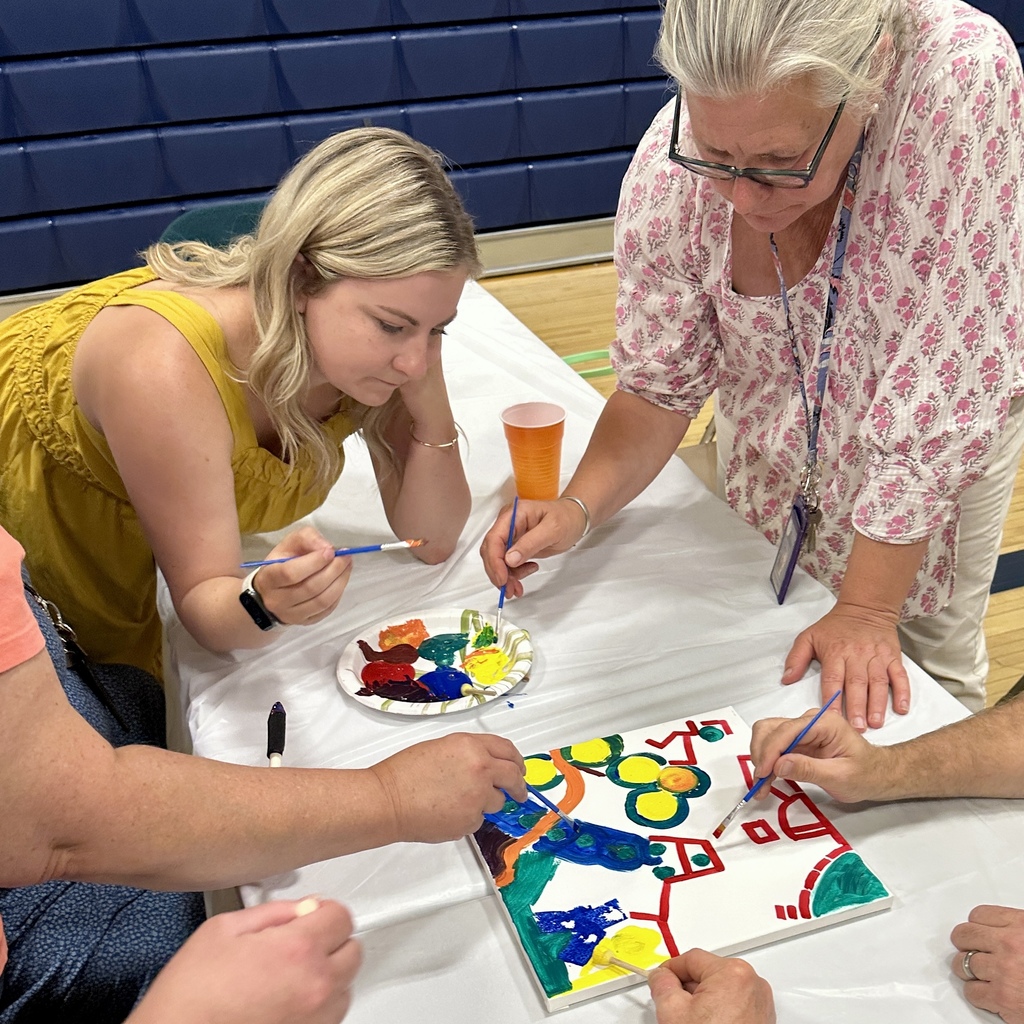 Two women painting a colorful canvas with others around the table.