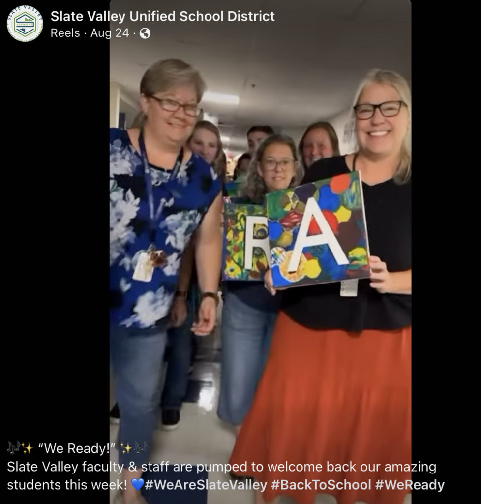 Group of Slate Valley faculty and staff smiling in a hallway, holding colorful painted canvases with the letters "R" and "A" as part of a back-to-school celebration.