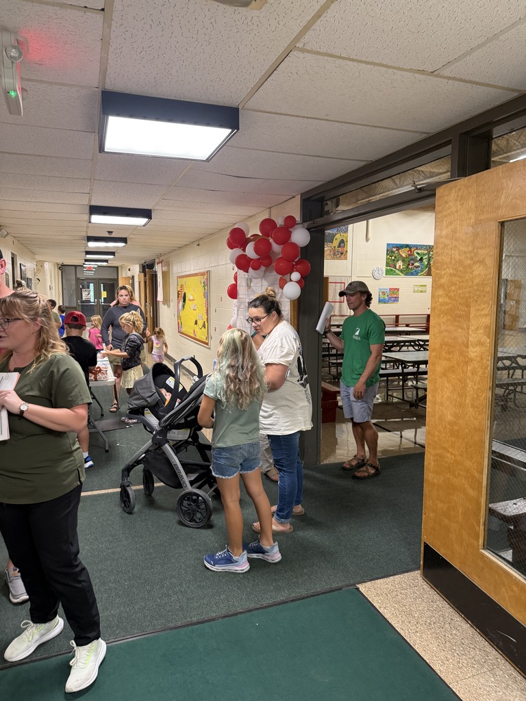 Families and children gather in a hallway decorated with red and white balloons.