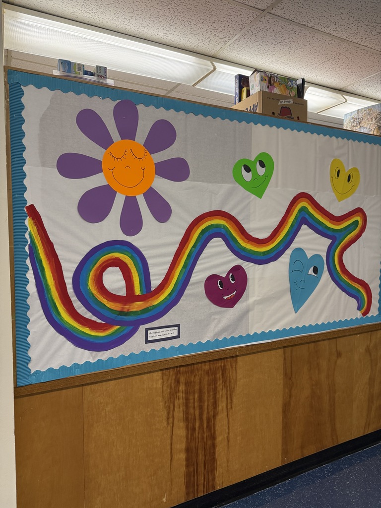 Bulletin board decorated with rainbows, hearts, and a smiling flower.