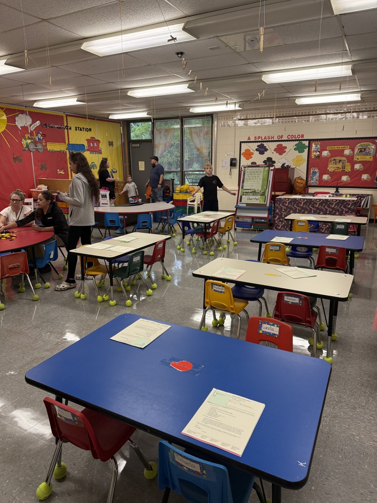 Classroom with small tables and colorful chairs set up for students, with families inside.