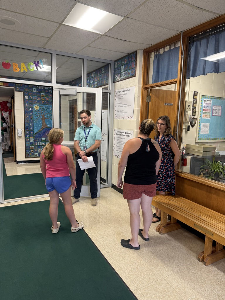 A teacher talks with a student and two adults in a school hallway near the office.