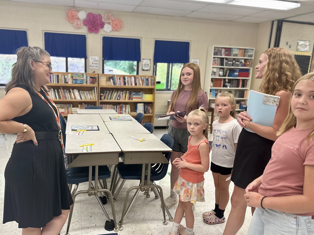Teacher in a black dress chats with a group of students and parents in a classroom lined with books.