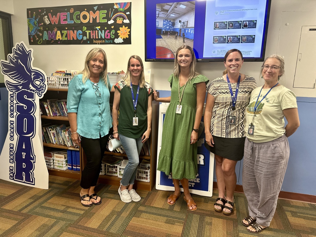 Group of five staff members stand smiling together in front of a “Welcome Amazing Things” sign.