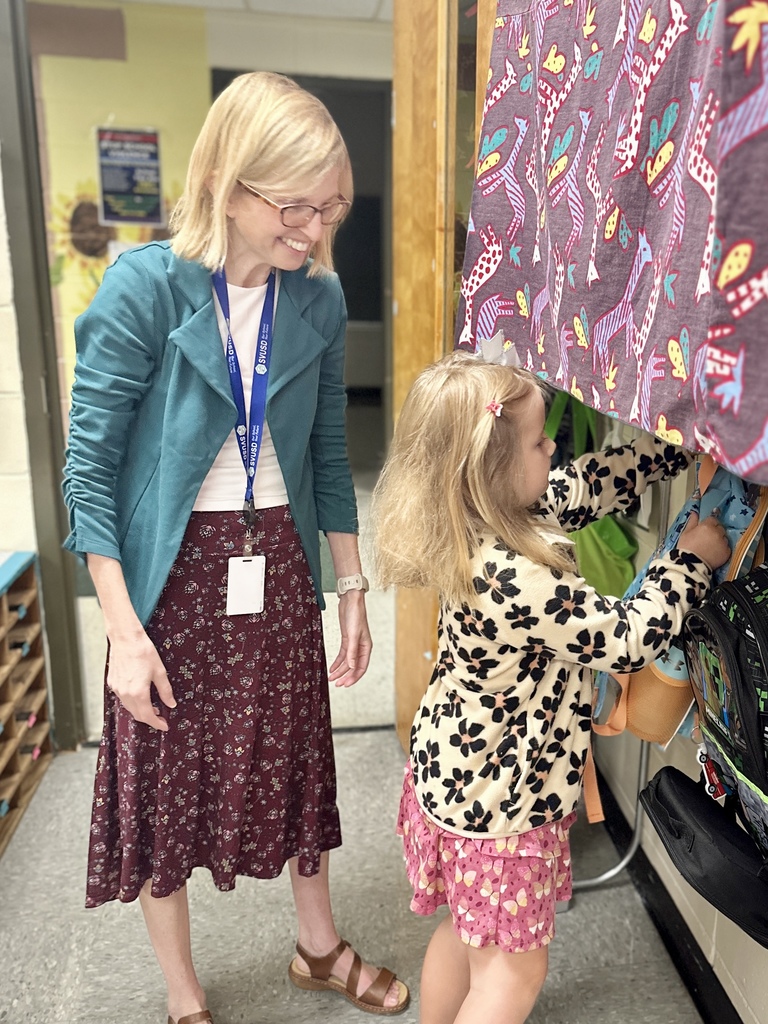 Teacher helps a student hang up their backpack in the classroom.
